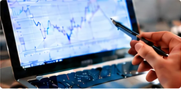 Hand mit Stift zeigt auf einen Chart auf dem Laptop
