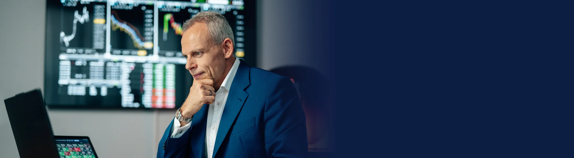 Mike Seidl im Anzug am Schreibtisch vor seinen Handelsmonitoren